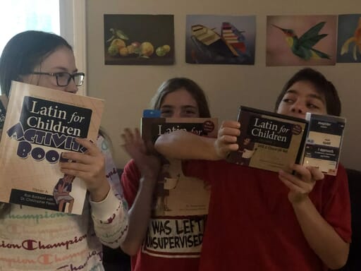 Latin for Children * Homeschool Curriculum Review Three kids with Latin for Children activity book, workbook, DVD video instuction, audio chants, and card game.